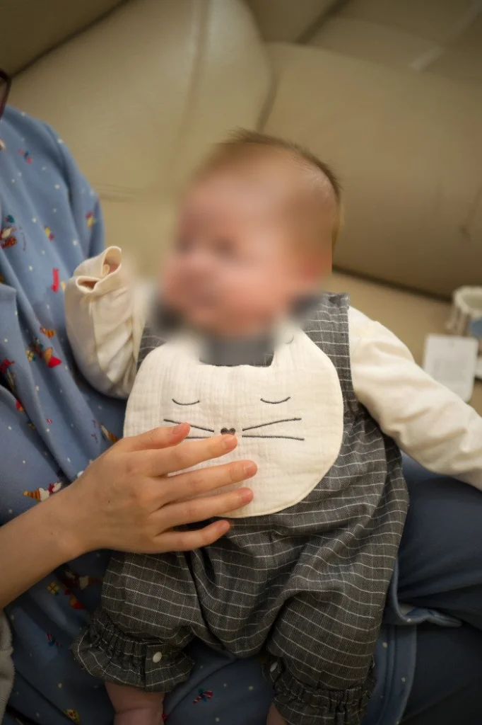 안겨서 앉아 있는 고양이 턱받이 차림의 아기