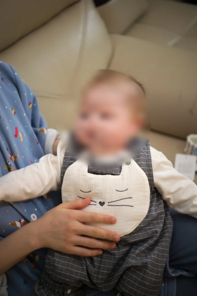 안겨서 앉아 있는 고양이 턱받이 차림의 아기