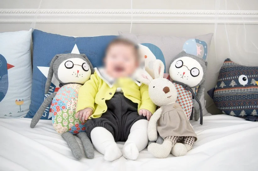노란 카디건을 입고 인형들 사이에 앉아 웃는 아기