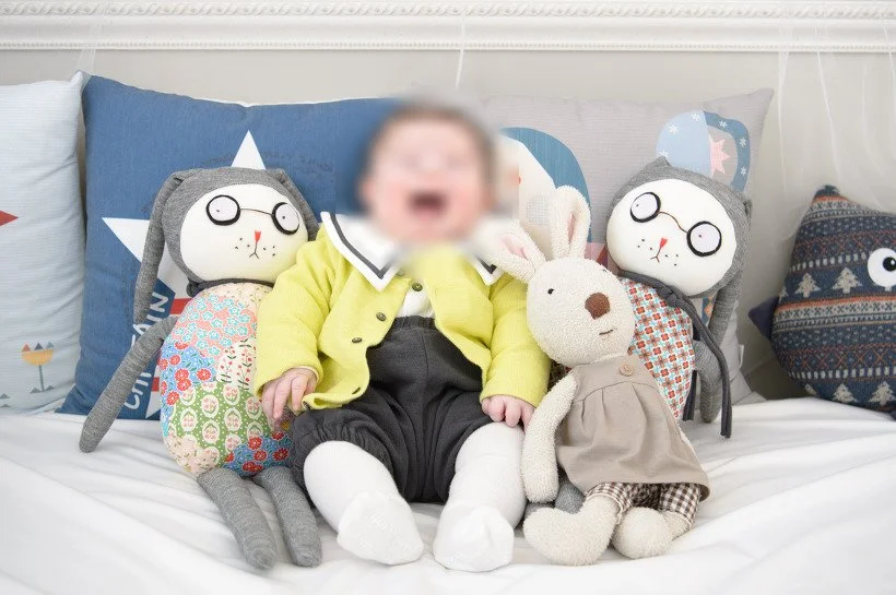 노란 카디건을 입고 인형들 사이에 앉아 웃는 아기