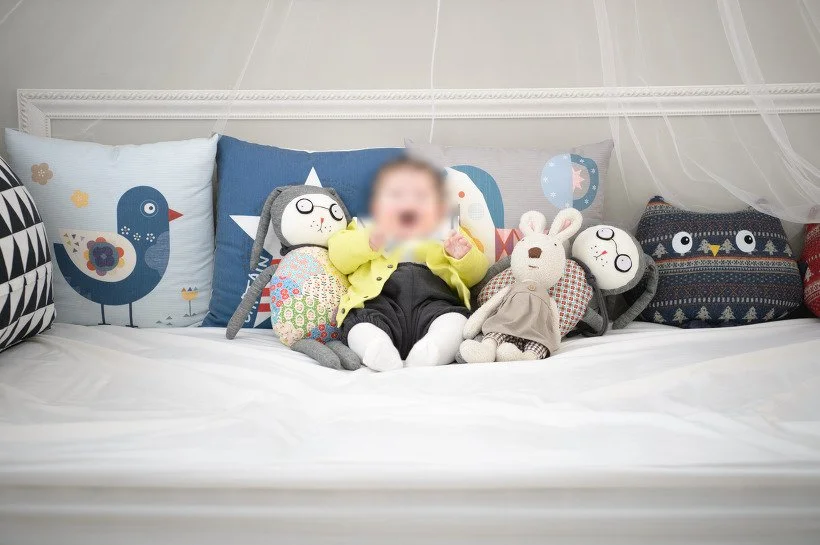 푸른 쿠션과 인형 사이에 앉은 아기