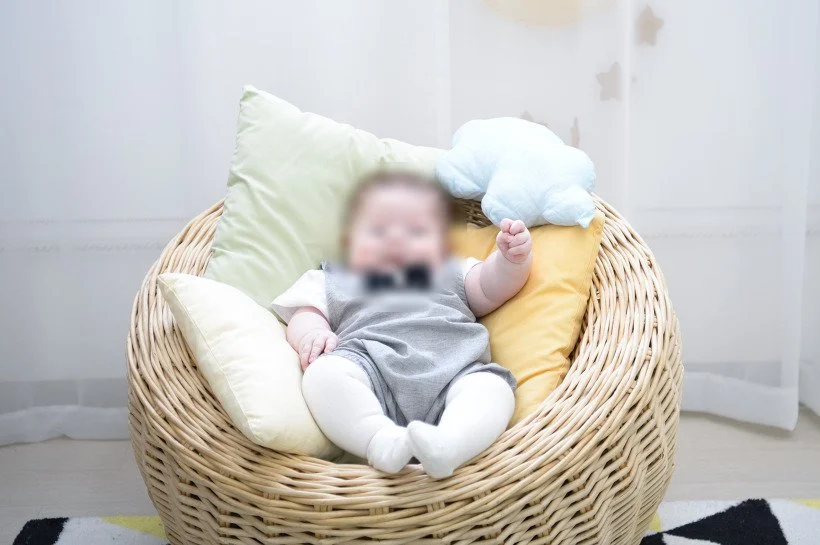 구름 쿠션을 든 채 라탄 의자에 누운 아기