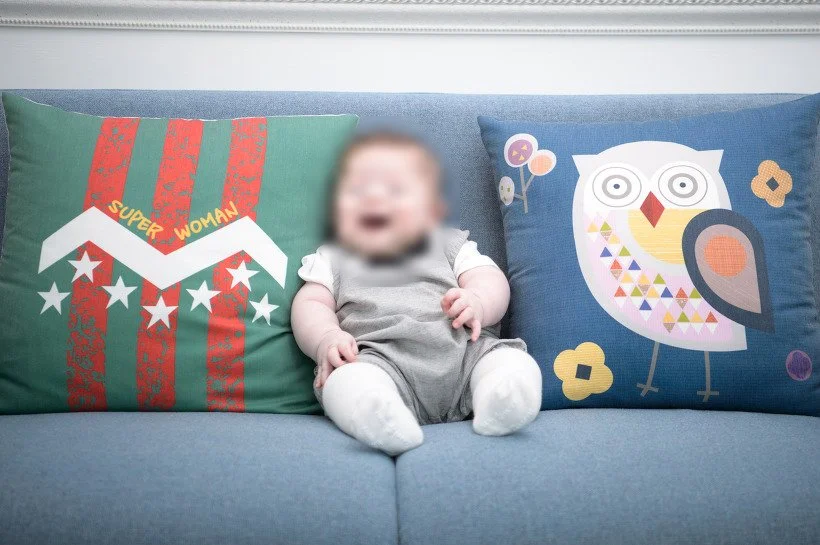 푸른 소파 위 쿠션 사이에 앉아 웃는 아기