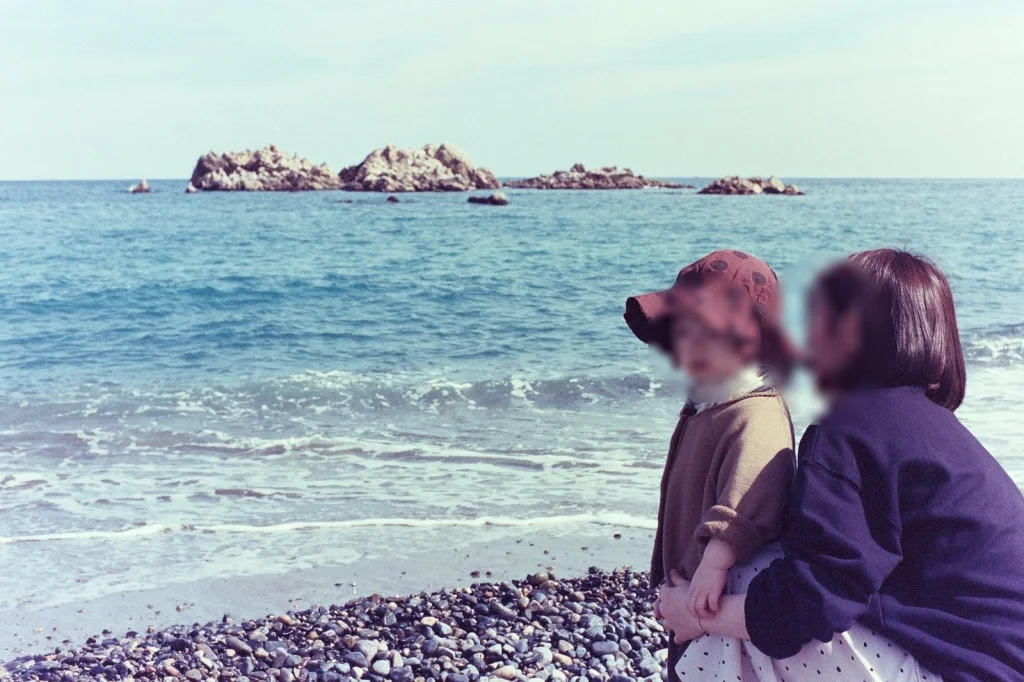 파도가 치는 해변에 아내와 쪼그려 앉은 아들