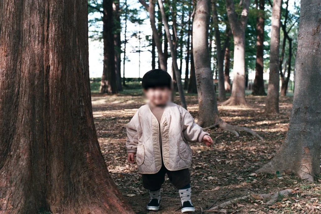 굵은 나무 사이 숲 바닥을 걷는 아들