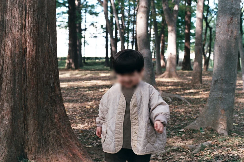 굵은 나무 사이 숲 바닥을 걷는 아들