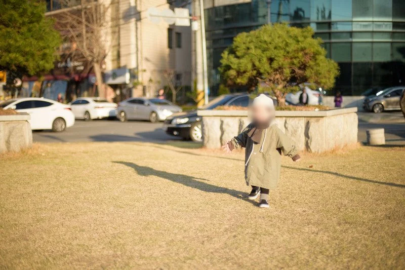 마른 잔디밭 위를 긴 그림자와 함께 달리는 아들
