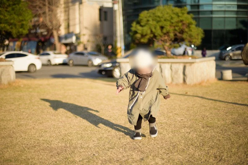 마른 잔디밭 위를 긴 그림자와 함께 달리는 아들