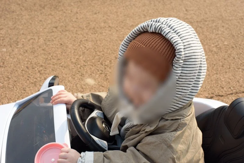 분홍 뚜껑을 쥐고 전동 자동차 운전석에 앉은 아들