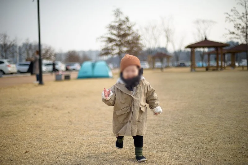 정자와 텐트가 보이는 공원 잔디밭을 걷는 아들