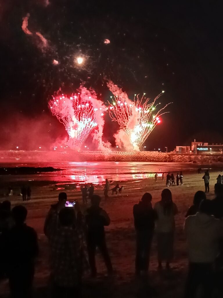 제방 쪽에서 붉은 불꽃 두 갈래가 솟고 해변에 선 사람들이 지켜보는 밤 해변