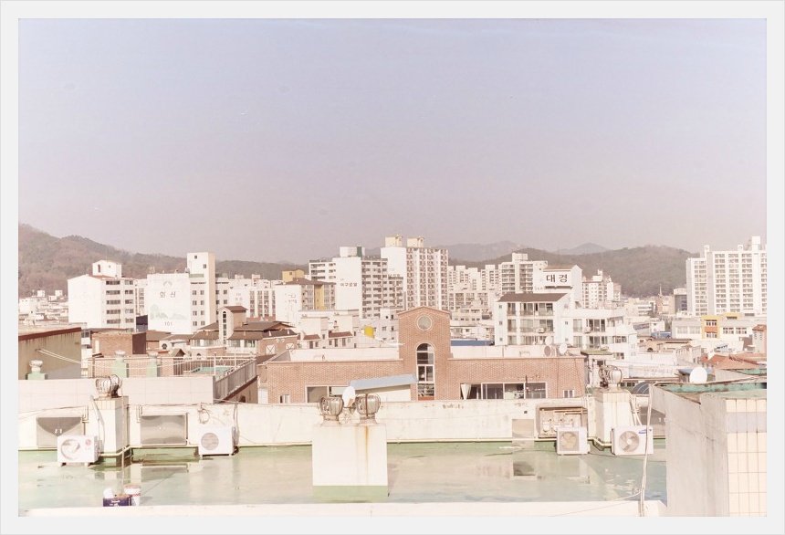 옥상 너머로 아파트와 건물이 빽빽한 동네 전경과 멀리 산 능선