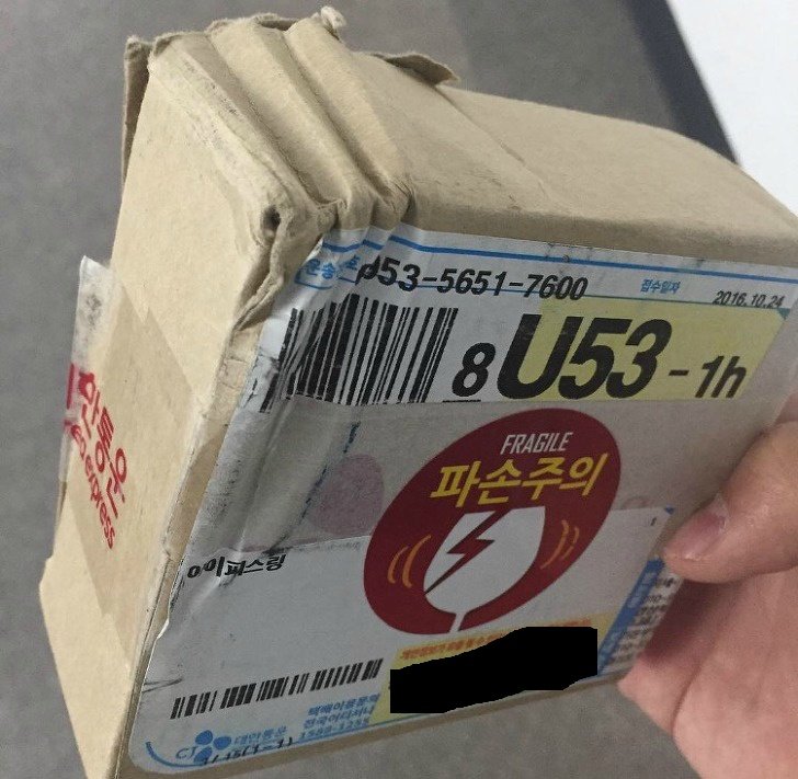 모서리가 찌그러지고 파손주의 스티커가 붙은 택배 상자와 송장