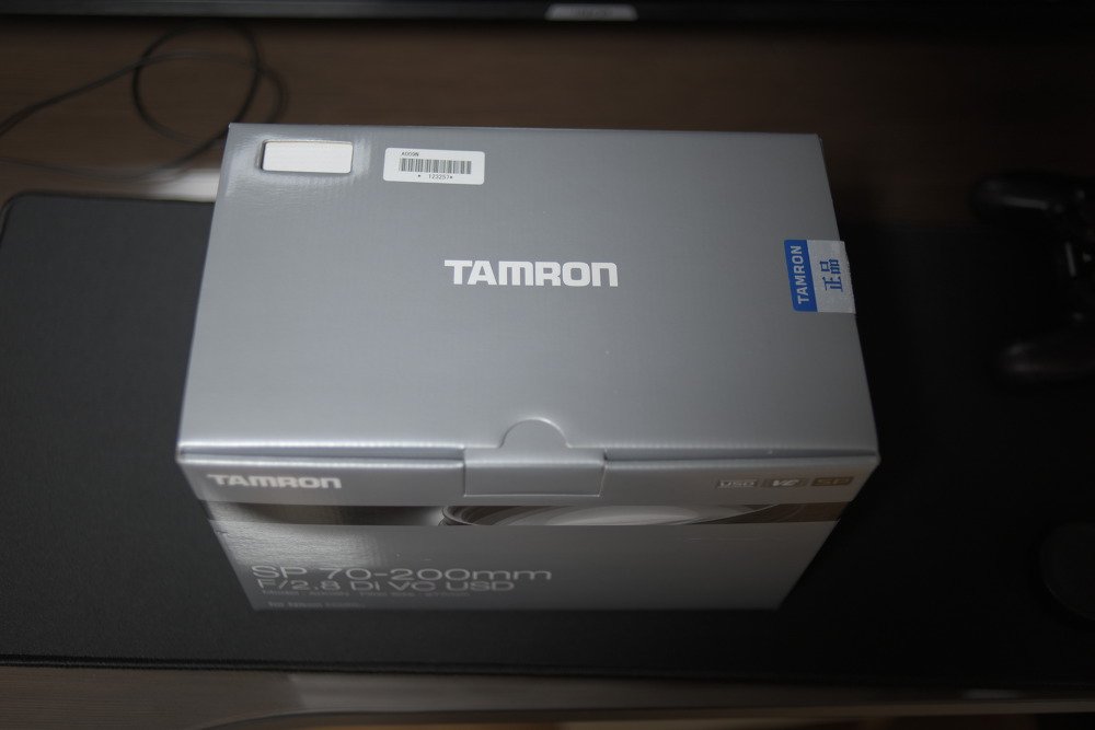 어두운 곳에 놓인 TAMRON 렌즈 상자와 윗면의 바코드 스티커