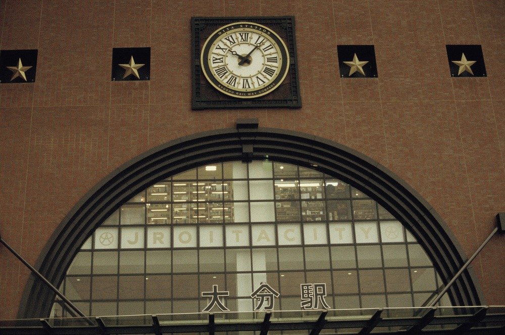 붉은 벽돌 외벽에 걸린 로마 숫자 시계와 별 장식, 아래쪽의 JR OITA CITY 글자와 大分駅 간판