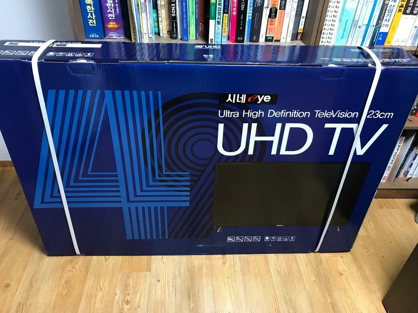 책장 앞에 세워 둔 시네아이 UHD TV 박스 앞면