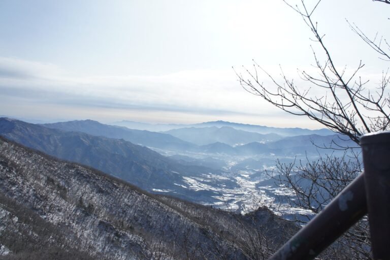 눈 덮인 비탈 아래로 골짜기와 겹겹의 먼 산이 보이는 능선 조망