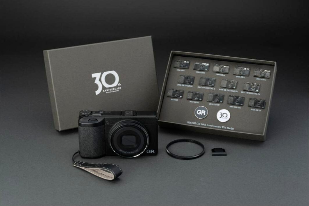 리코 GR IV 30주년 기념 에디션 키트 구성품 — 카메라 정면, 30주년 로고 상자, 핀 배지 16종, 가죽 핑거 스트랩, 링캡, 핫슈 커버