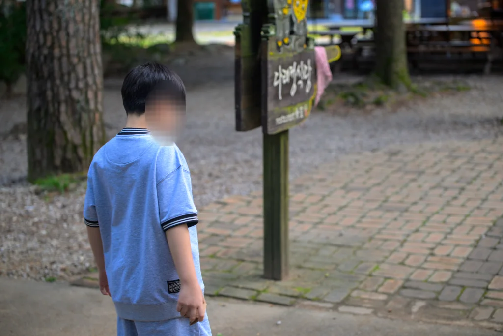 나무 기둥에 걸린 다래정식당 안내판 옆을 지나가는 아이