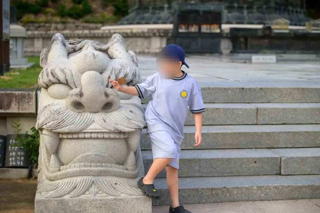 큰 돌짐승 석상의 코를 만지며 계단을 오르는 아이