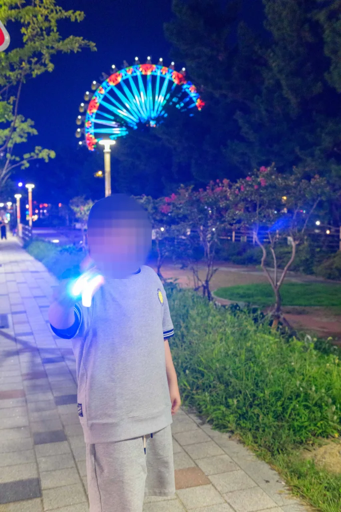 밤 산책로에서 파랗게 빛나는 장난감을 든 아이와 뒤편 대관람차