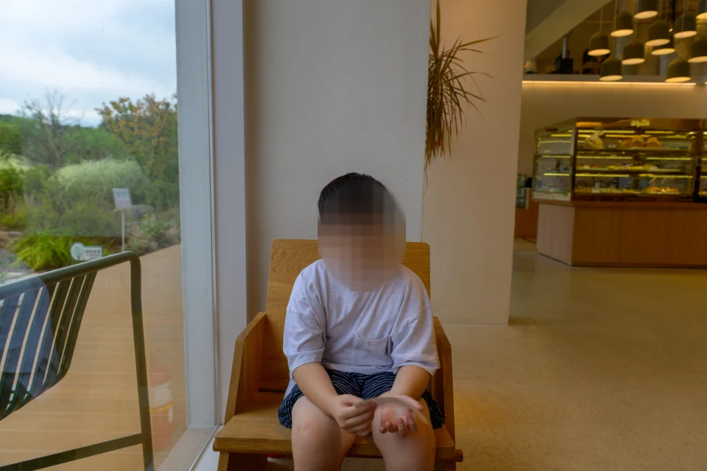 통창 옆 나무 의자에 앉은 아이와 뒤편 빵 진열장