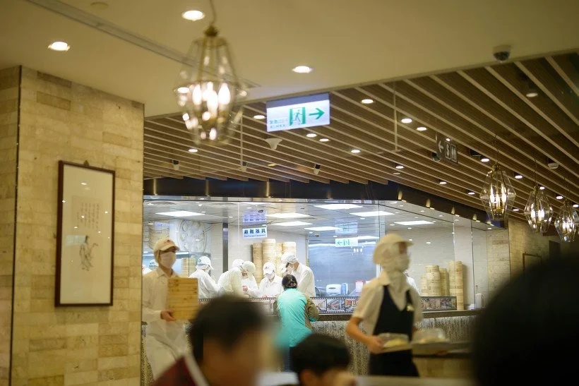식당 안 유리 너머 주방에 흰 모자와 흰 옷을 입은 사람들이 서 있는 모습, 앞쪽 두 사람은 얼굴을 가림