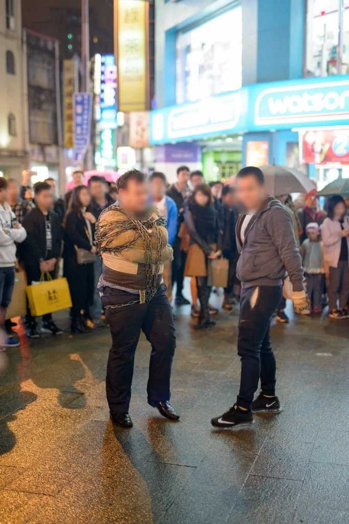 젖은 밤거리에서 두 사람을 사람들이 둘러싼 모습, 두 사람의 얼굴을 가림 (세로 사진)