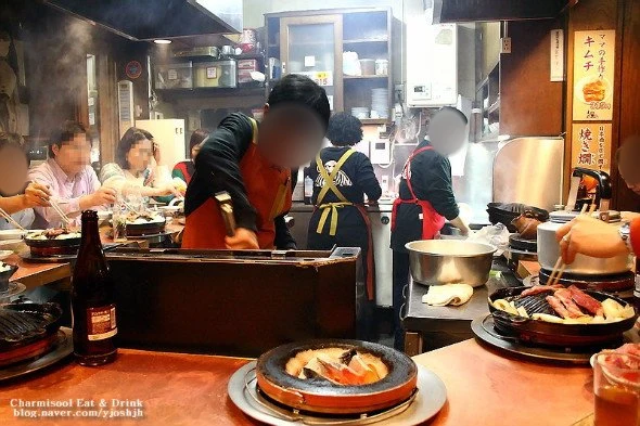 주방과 카운터에서 일하는 사람들과 앉은 손님들, 얼굴은 흐림 처리