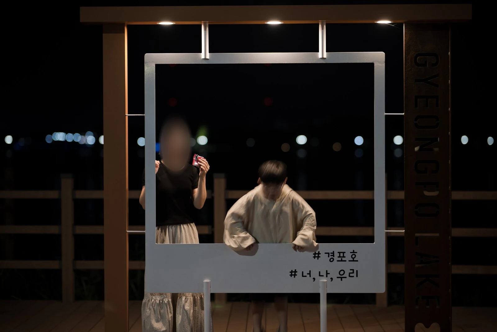 '#경포호' 글자가 적힌 흰 사진 틀 안에 선 어른과 아이, 어른 얼굴은 가림 처리