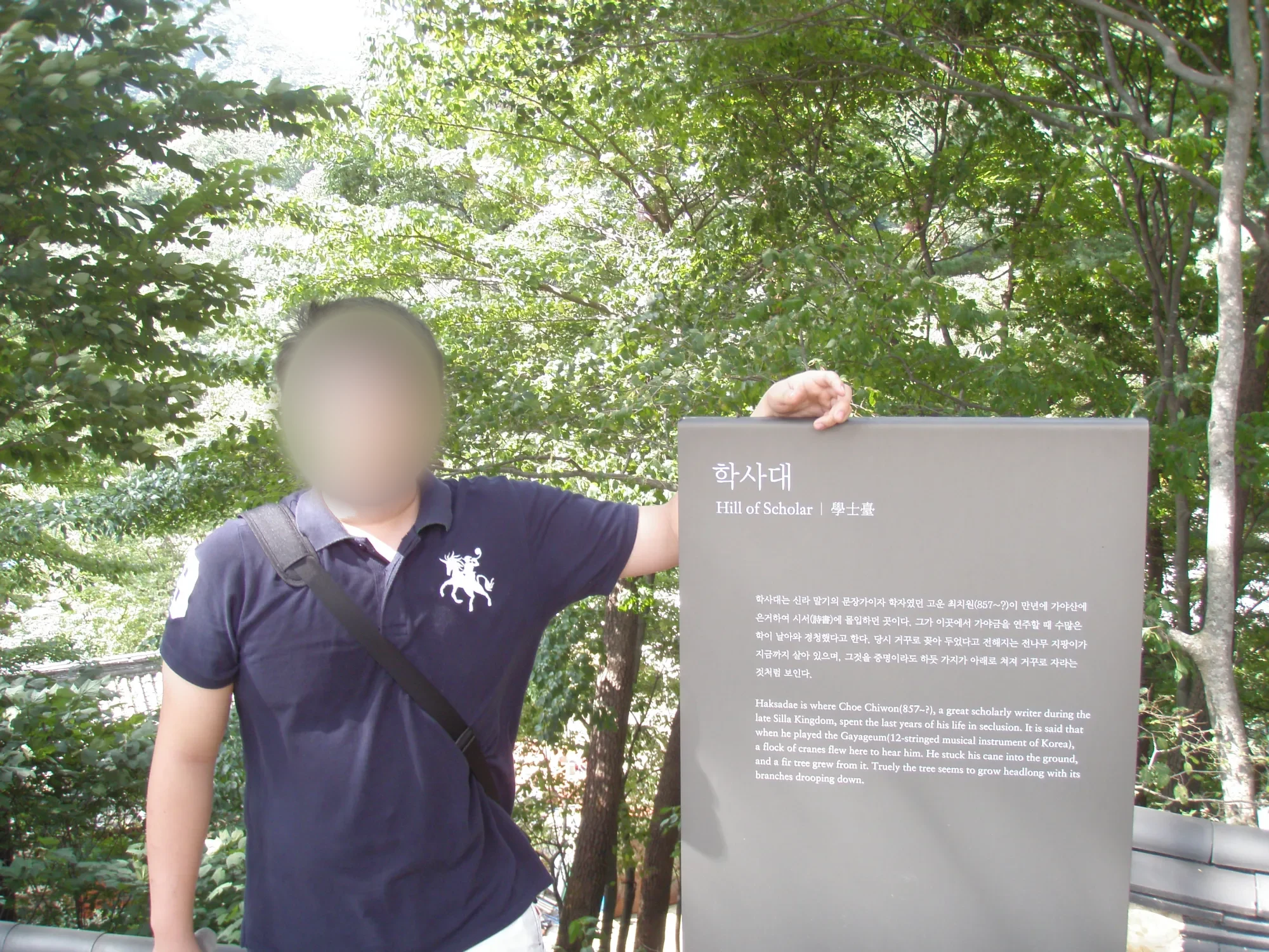 학사대 표지판 옆에 선 짙은 남색 셔츠의 남자 어른, 얼굴은 흐리게 처리했고 표지판에 한글과 영문 설명이 적혀 있다