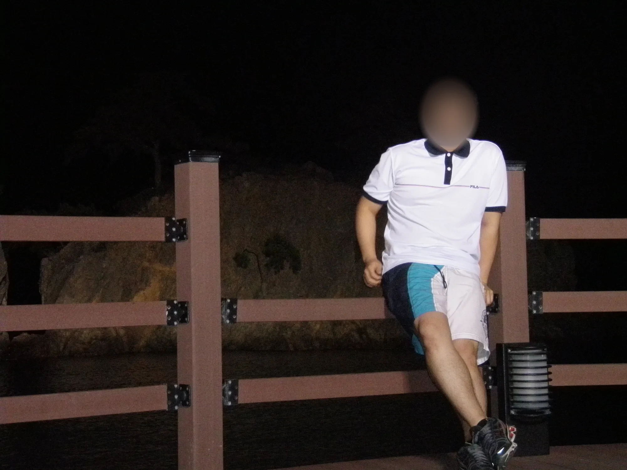 밤에 나무 난간에 기대 선 남자(얼굴 흐림)와 뒤쪽의 어두운 바위 윤곽을 찍은 사진