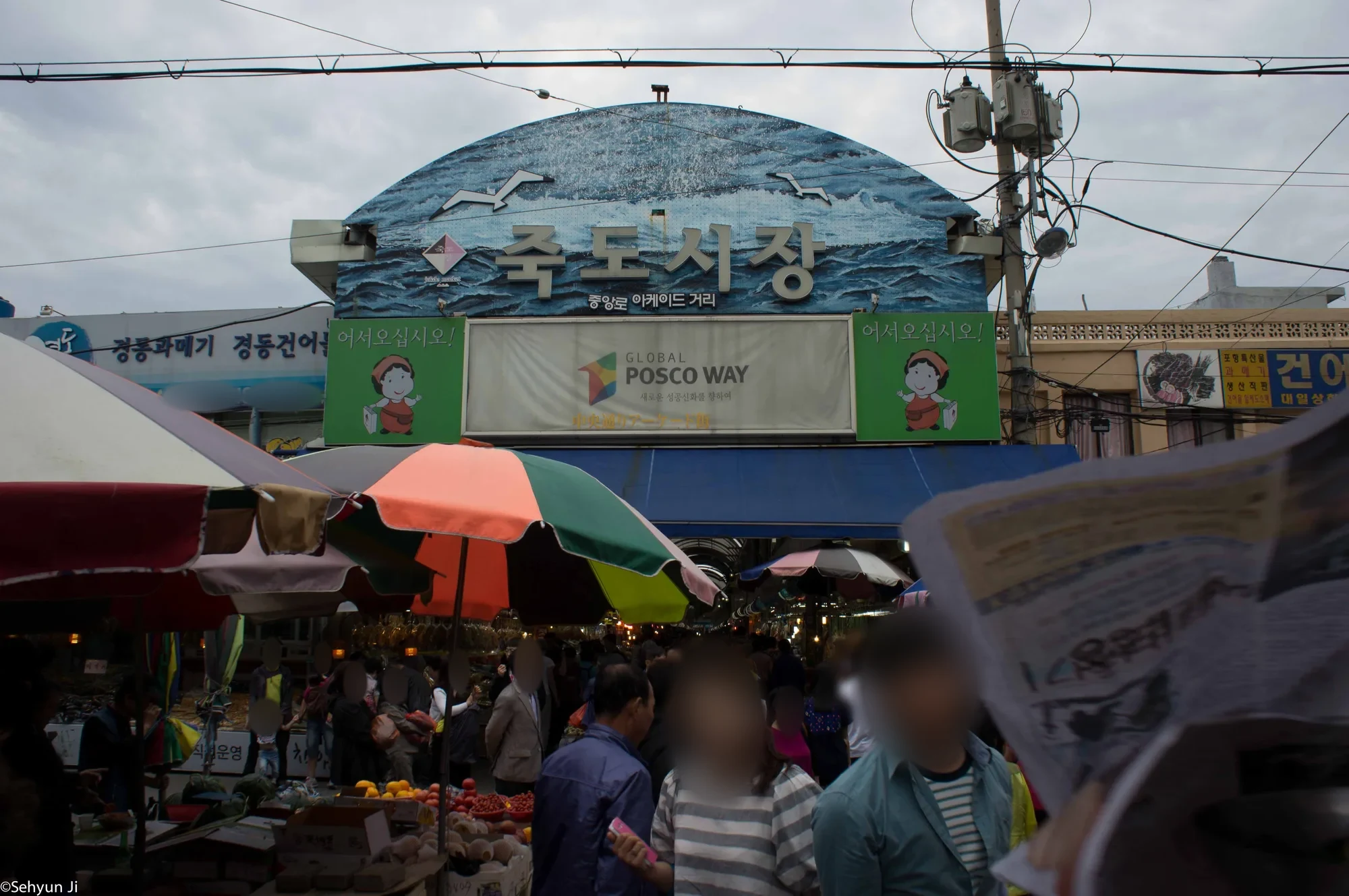 아치형 간판에 '죽도시장'이 적힌 시장 입구와 파라솔 아래에 모인 사람들