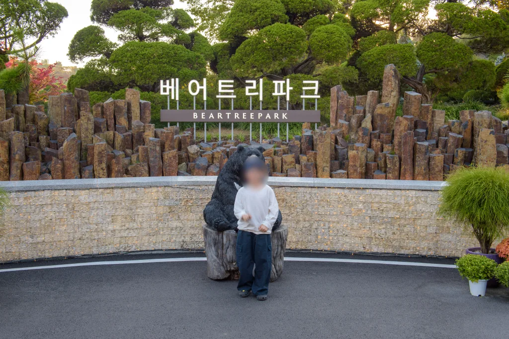 베어트리파크 간판 앞 검은 곰 조각상 옆에 서 있는 아들