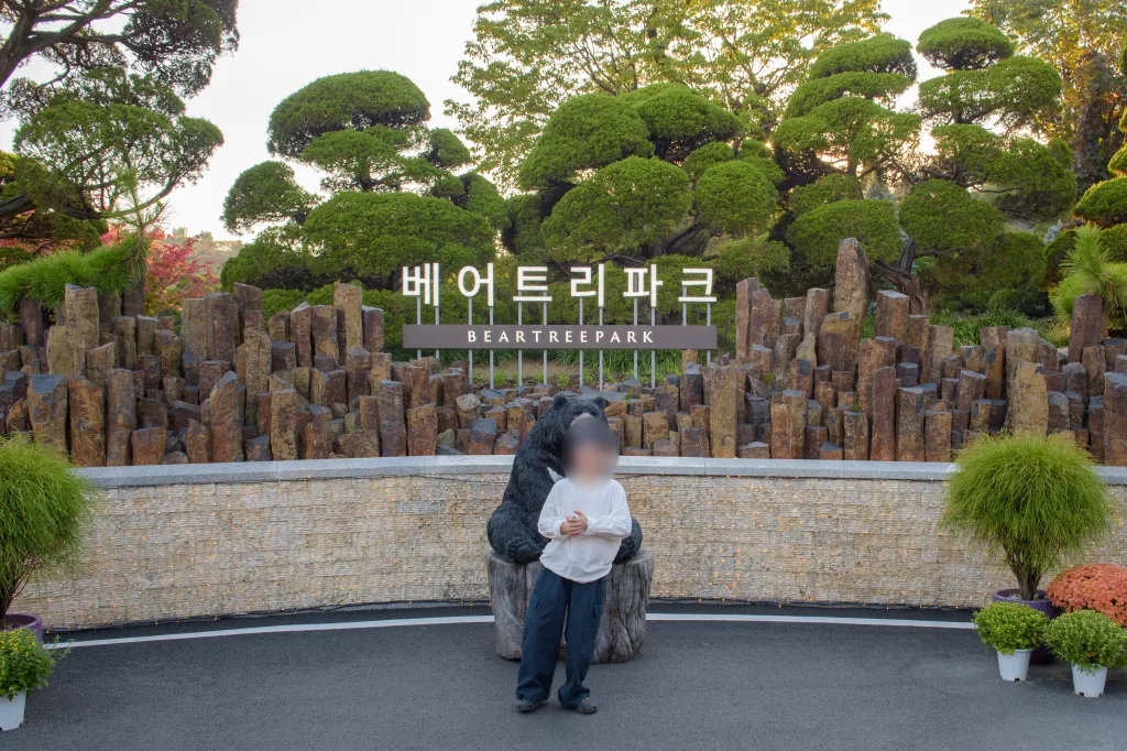 같은 간판 앞에서 곰 조각상 쪽으로 붙어 선 아들