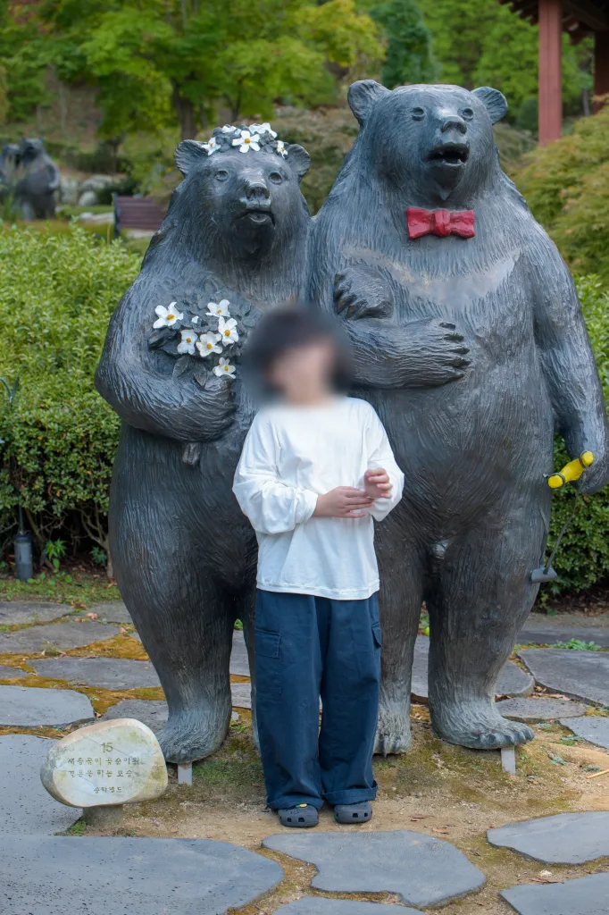 꽃 머리띠를 쓴 청동 곰 한 쌍 앞에 서 있는 아들
