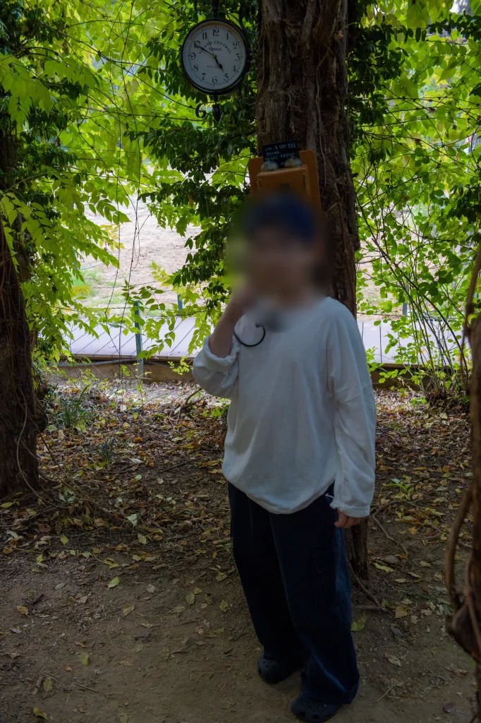 시계가 걸린 나무 아래에서 한 손을 얼굴 옆에 올린 아들
