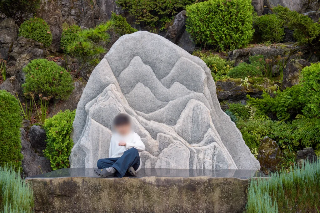 산 모양을 새긴 하얀 돌 앞 석재 받침에 다리를 꼬고 앉은 아들