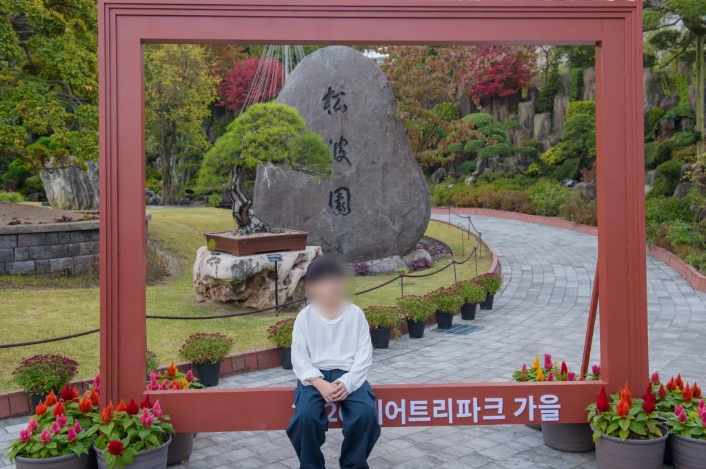 붉은 액자 프레임 안에서 앉은 아들과 뒤의 松波園 바위