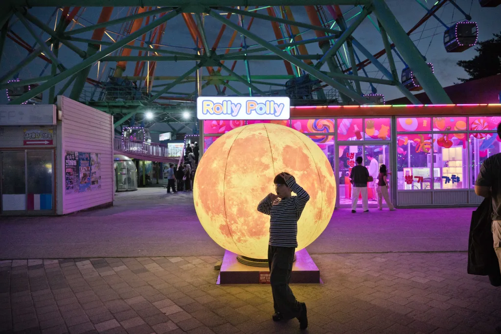 Rolly Polly 간판 앞 둥근 달 조형물 앞에 실루엣으로 서 있는 아들