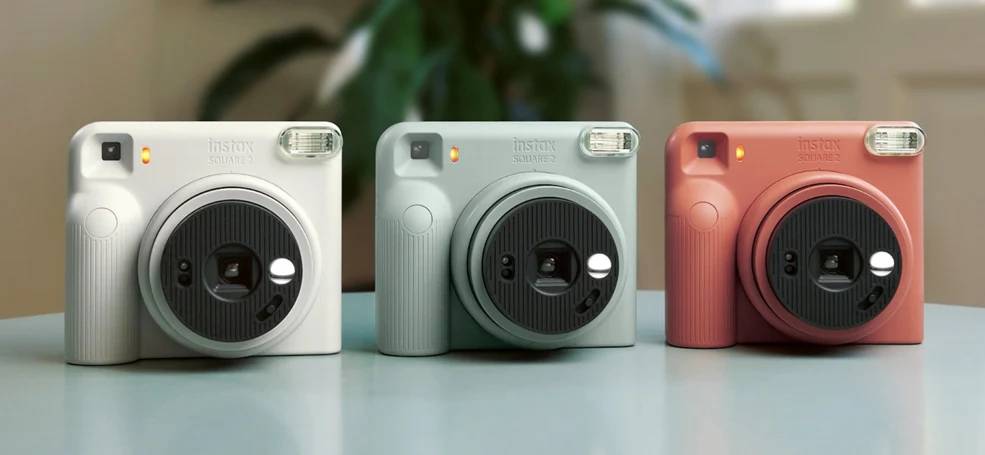 instax SQUARE 2 미스티 화이트·슬레이트 블루·브릭 레드 세 대가 탁자 위에 나란히 놓인 모습