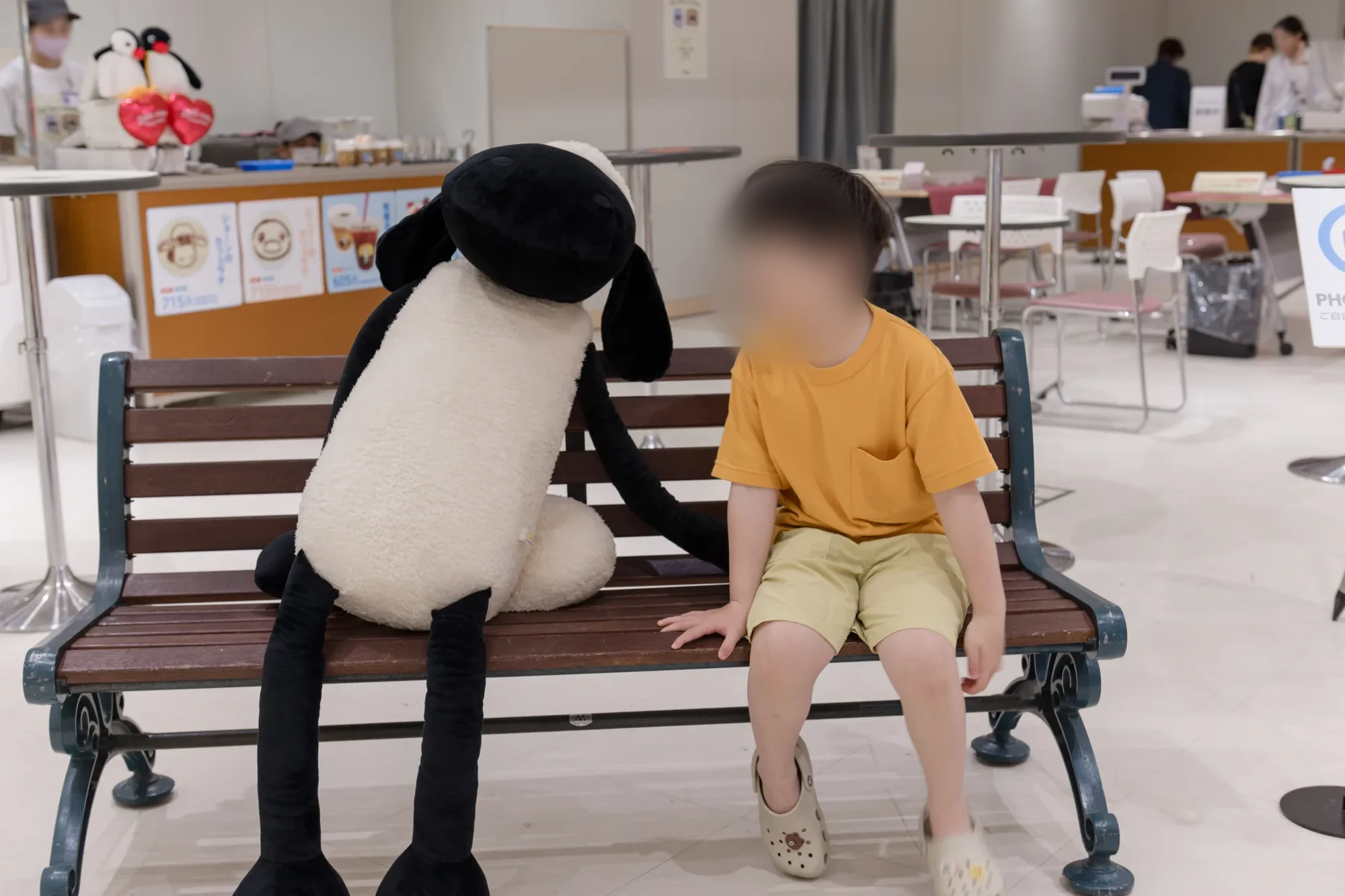벤치에서 인형 쪽으로 고개를 돌린 노란 티셔츠의 아이와 벤치 위로 늘어진 인형의 검은 팔