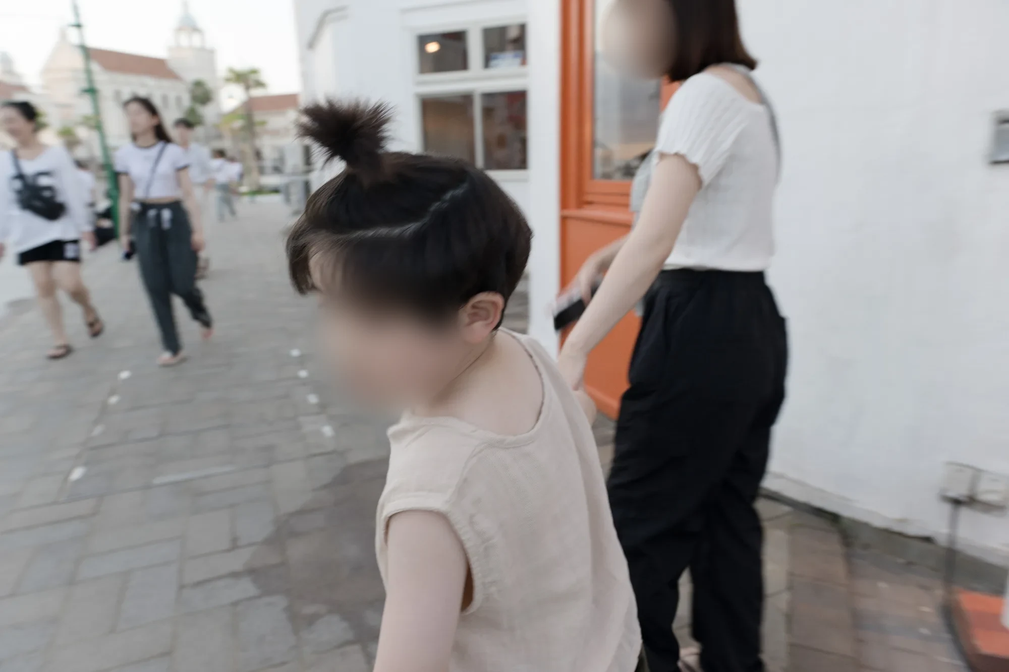 흰 벽 건물 옆 포장된 산책로에서 고개를 돌린 아들과 그 옆을 걷는 아내