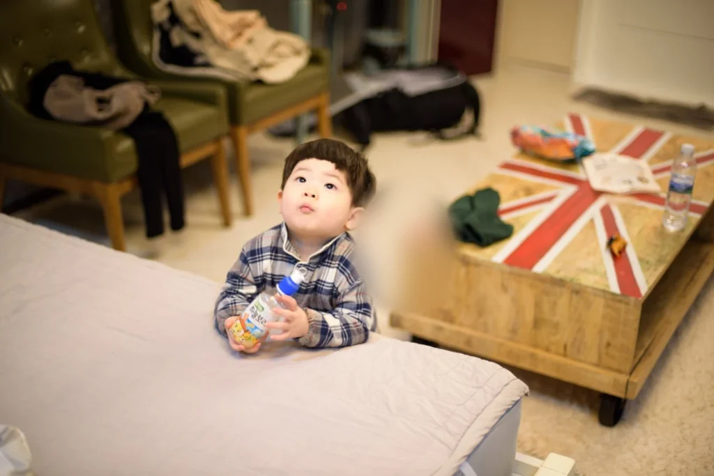 펜션 방 침대 옆에서 병을 쥐고 있는 아이(얼굴 가림)