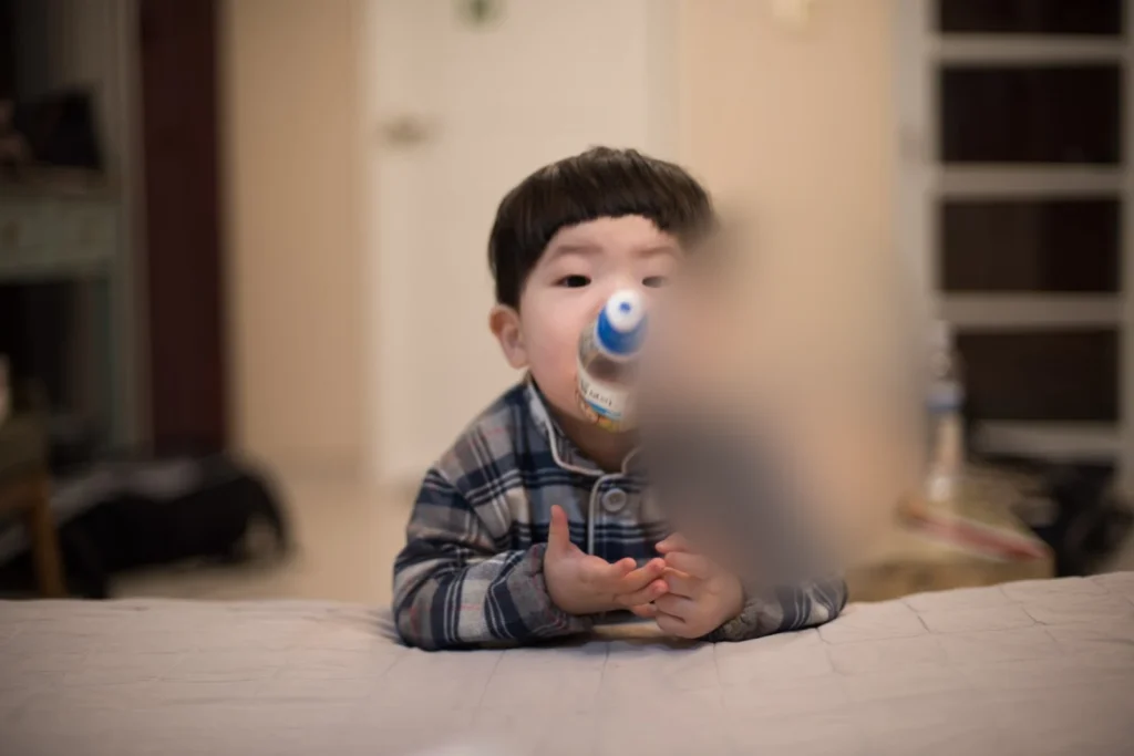 침대 가장자리에 팔을 얹고 병을 입에 댄 아이(얼굴 가림)
