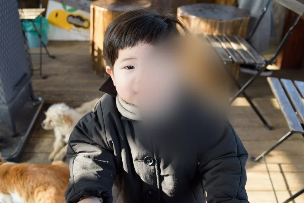 카메라를 향해 선 아이, 아래쪽에 동물 두 마리가 보인다(얼굴 가림)