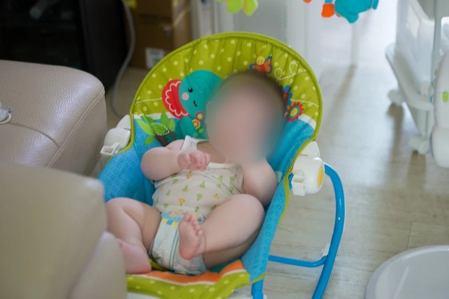 바운서 의자에 앉아 손을 가슴 앞에 모은 아기, 얼굴을 가림