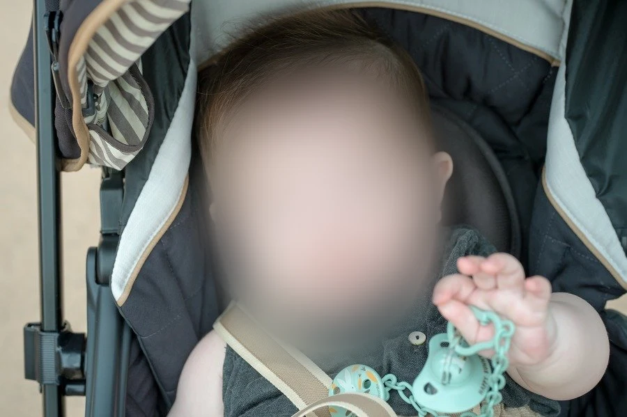 유모차 안에서 청록색 쪽쪽이 고리를 손에 쥔 아기를 가까이서 찍은 사진, 얼굴을 가림