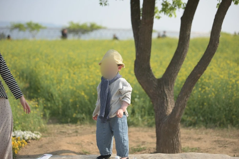 노란 꽃밭 앞에서 모자를 쓰고 푸른 스카프를 두른 아이, 얼굴을 가림