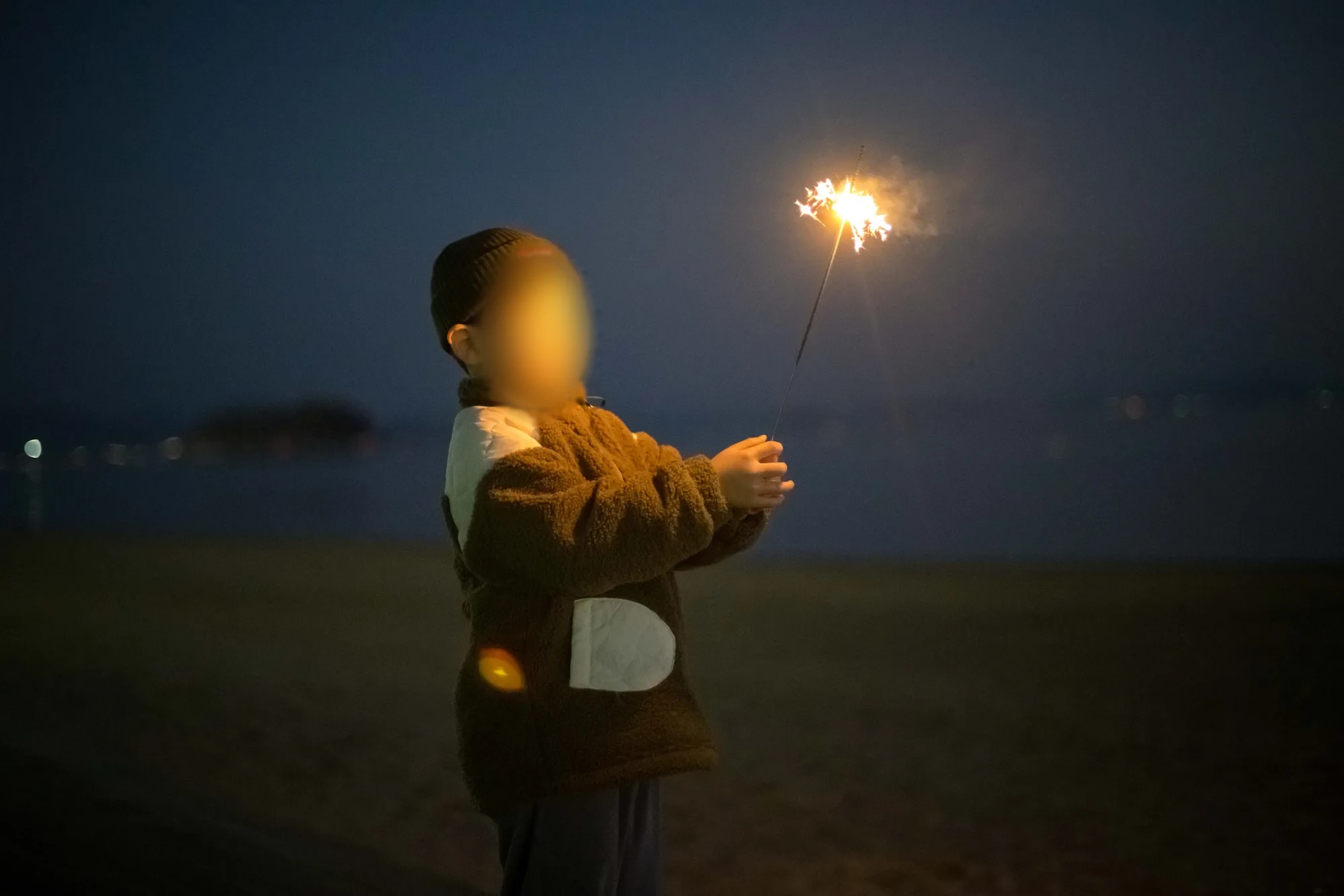 어두운 해변에서 불꽃이 타는 막대를 든 아이, 얼굴을 가림